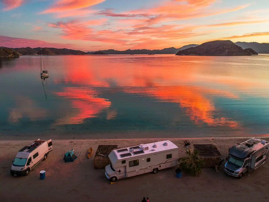three campers parked on a beach at sunset